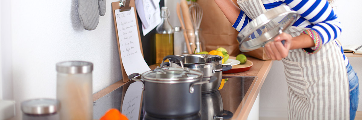 Une jeune femme lit des instructions dans sa cuisine en tenant le couvercle d'une casserole 