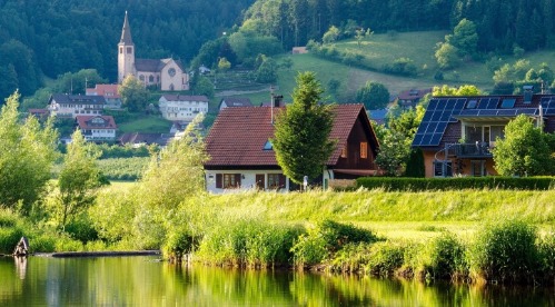 Deux maisons dont l'une avec des panneaux photovoltaïques devant un lac pendant le printemps avec un paysage vert. 