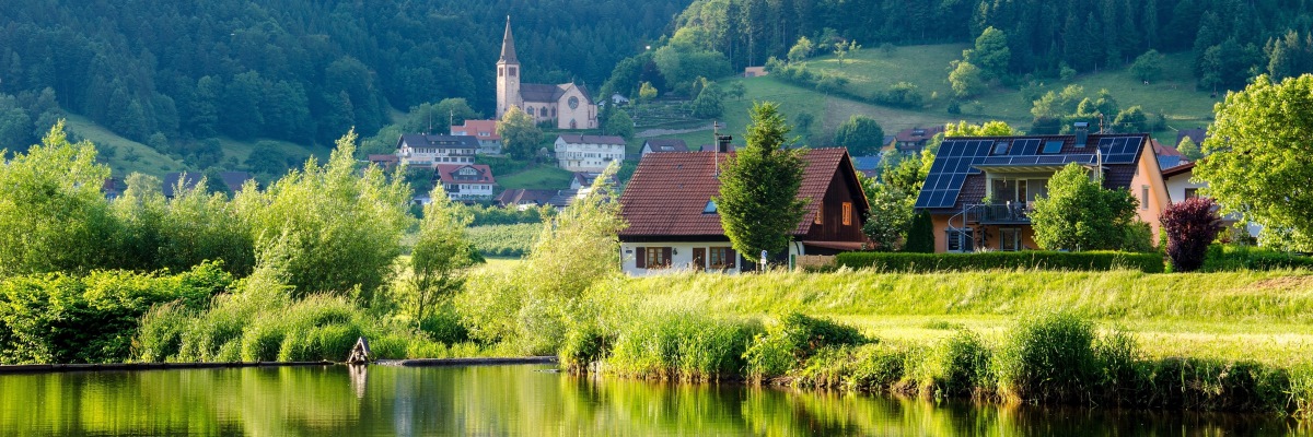 Deux maisons dont l'une avec des panneaux photovoltaïques devant un lac pendant le printemps avec un paysage vert. 