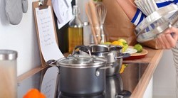 Une jeune femme lit des instructions dans sa cuisine en tenant le couvercle d'une casserole 